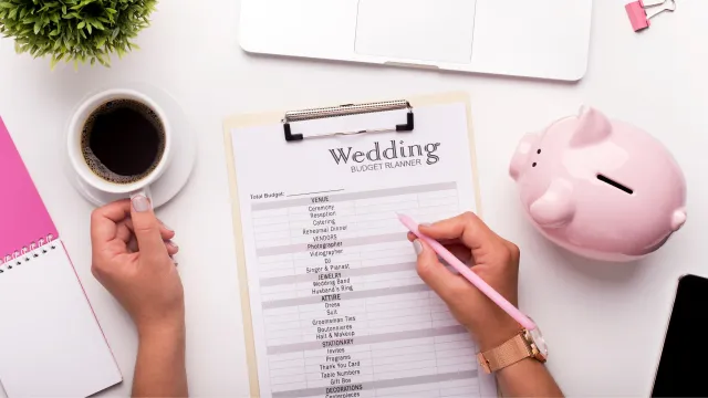Spreadsheet on a clipboard titled 'Wedding Budget Planner' for planning wedding photography on a budget